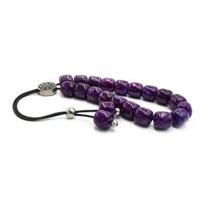 May include: A purple prayer beads necklace with a silver clasp. The beads are made of a speckled material and are strung on a black cord.