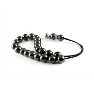 Puede incluir: Un collar mala de cuentas de hematites negras con un cierre plateado y un cord&oacute;n negro.