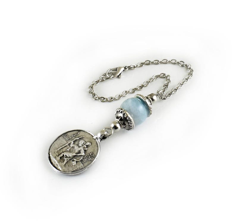 Puede incluir: Una pulsera de cadena de metal plateado con una cuenta de piedra preciosa azul claro acentuada con tapas plateadas ornamentadas y un colgante circular que representa en relieve una figura sentada. Incluye un cierre de mosquet&oacute;n.