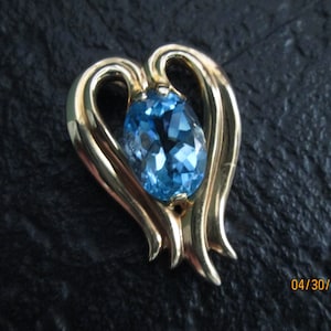 May include: A gold heart-shaped pendant with a blue topaz gemstone in the center.