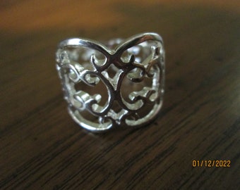 May include: A silver ring with a delicate, intricate design. The ring is made of a thin metal and has a wide band.
