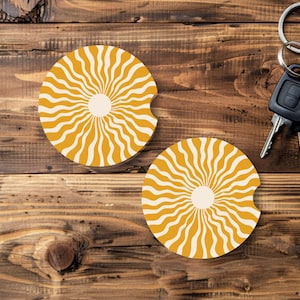 May include: Two yellow and white car coasters with a sunburst design. The coasters are round with a small notch on one side. A set of car keys with a black fob are also in the image.