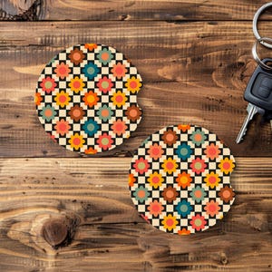 May include: Two round car coasters with a retro floral design. The coasters feature a cream background with a black and white checkerboard pattern and colorful flowers in shades of orange, pink, blue, and yellow. A car key is in the background.