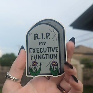 May include: A gray tombstone sticker with the text "R.I.P. My Executive Function" and two purple flowers.