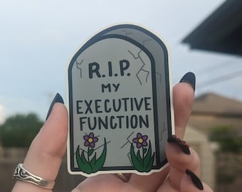 May include: A gray tombstone sticker with the text "R.I.P. My Executive Function" and two purple flowers.