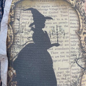 May include: A decorative pillow featuring a silhouette of a witch in a hat and dress, set against a vintage newspaper print background. The pillow has a cream-colored border and is embellished with fabric accents. The design evokes a Halloween or gothic theme.