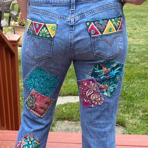 May include: Blue denim jeans with colorful embroidered patches on the back pockets and patchwork on the legs.