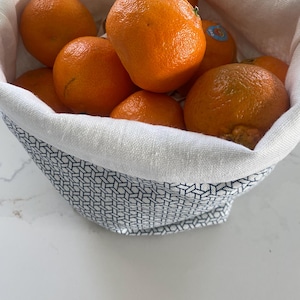 May include: A white fabric bag with a blue geometric pattern, filled with a variety of orange citrus fruits.