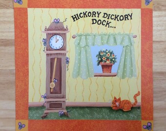 May include: A yellow and orange illustrated wall art print with a grandfather clock, a cat, and a window with a plant. The text "Hickory Dickory Dock..." is written in black at the top of the print.