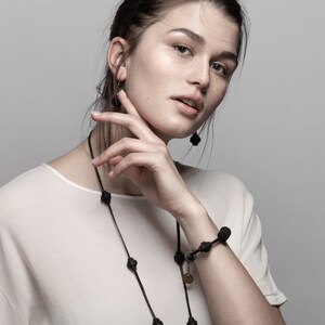May include: A woman wearing a white shirt with a black necklace and bracelet. The necklace and bracelet are made of black beads.