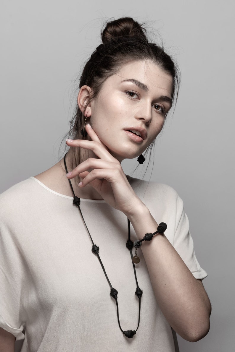 May include: A woman wearing a white shirt with a black necklace and bracelet. The necklace and bracelet are made of black beads.
