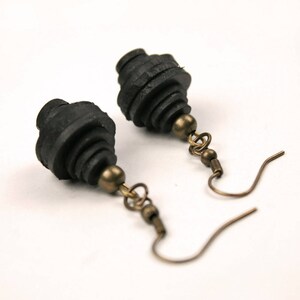 May include: A pair of black dangle earrings with a layered, geometric design. The earrings are made of black paper and have a bronze hook.