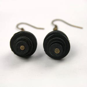 May include: A pair of black leather earrings with a gold dot in the center of each earring. The earrings are made of stacked circles of leather.