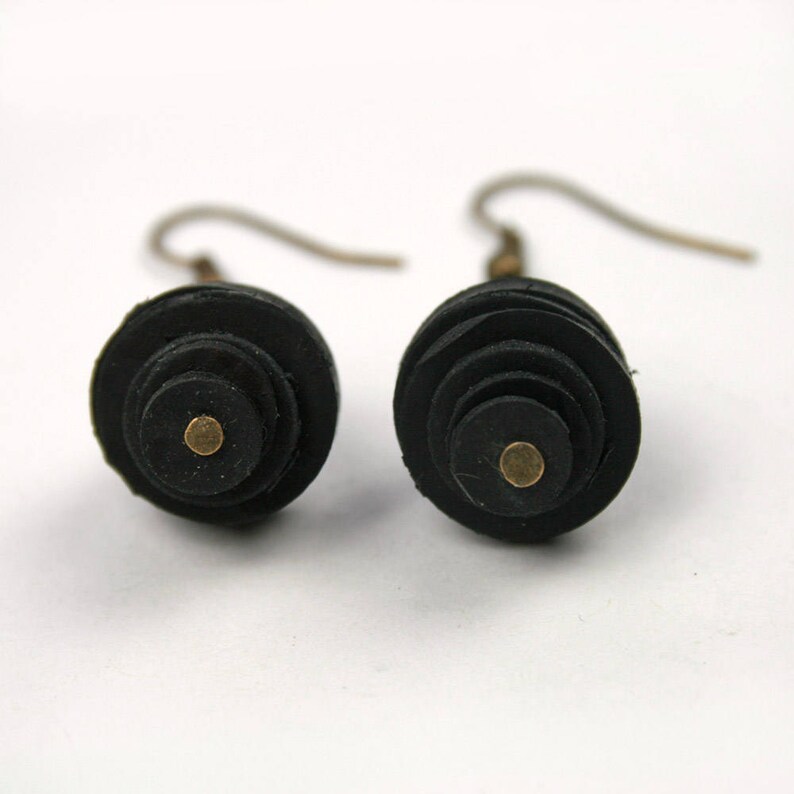 May include: A pair of black leather earrings with a gold dot in the center of each earring. The earrings are made of stacked circles of leather.