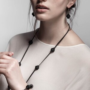 May include: A woman wearing a white top with a black necklace and bracelet. The necklace and bracelet are made of layered black circles.