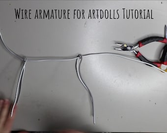 May include: A close-up of a wire armature for art dolls. The armature is made of thin, silver wire and is shaped like a human body. The wire is twisted together at the shoulders, hips, and knees. A pair of pliers is lying on the table next to the armature.