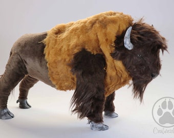 Könnte beinhalten: Handgefertigte Bison-Skulptur mit detailliertem Design. Das Bison hat einen braunen Körper, eine zottelige, braun-beige Mähne und kleine, gebogene Hörner. Die Skulptur ist in einer stehenden Position dargestellt, die Beine leicht angewinkelt.