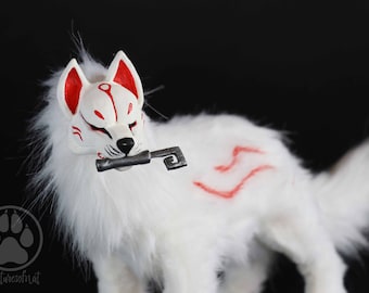 Op de afbeelding: Een witte, pluche wolf figuur met rode markeringen en een decoratief masker. De wolf houdt een zilveren sleutel in zijn bek. Het beeldje heeft een zachte textuur en staat tegen een zwarte achtergrond.
