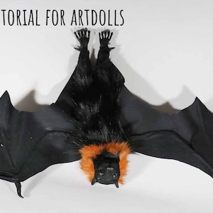 Könnte beinhalten: Eine handgefertigte Fledermausflügel-Requisite für Kunstpuppen. Die Flügel sind schwarz mit einer pelzigen schwarzen und orangefarbenen Brust und Kopf. Der Text "BAT WING TUTORIAL FOR ARTDOLLS" steht oben. Das Logo "Creatures of Nat" befindet sich oben rechts.