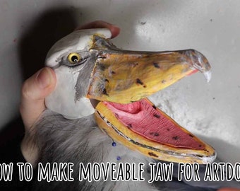 May include: A close-up of a bird-like art doll head with an open beak. The beak is yellow and brown, with a pink interior. The eye is yellow. The text "HOW TO MAKE MOVEABLE JAW FOR ARTDOLLS" is at the bottom.