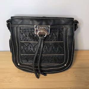 May include: Black leather crossbody bag with a silver clasp and the word "CHAPS" embossed on the front. The bag has a woven pattern and a fringe detail.