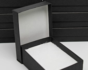 Puede incluir: Una pila de cajas de cartón negras con una sola caja abierta, revelando un interior blanco. Las cajas son ideales para empaquetar artículos pequeños.
