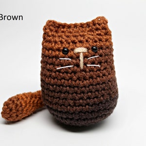 May include: A handmade crochet cat in shades of dark brown. The cat has black eyes, white whiskers, and a beige nose. The text "Dark Brown" is in the upper left corner. The cat has a small tail.