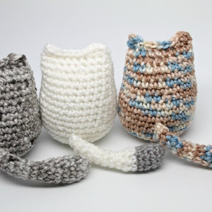May include: Three handmade crochet cat toys in gray, white, and a mix of blue and brown. Each cat toy has a tail and a rounded body with pointed ears. The toys are displayed on a white background.