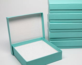 May include: A stack of teal blue gift boxes with one box open and empty. The open box is a light teal blue with a white interior.