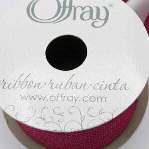 Pu&ograve; includere: Un rotolo di nastro di juta rosso borgogna con il nome del marchio Offray e l'indirizzo del sito web stampato sull'etichetta. L'etichetta include anche le parole "ribbon. ruban. cinta".