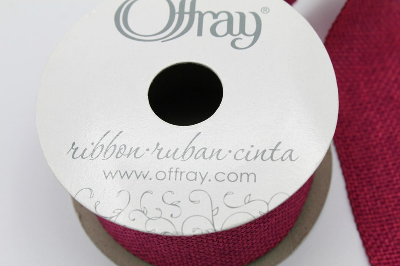 Pu&ograve; includere: Un rotolo di nastro di juta rosso borgogna con il nome del marchio Offray e l'indirizzo del sito web stampato sull'etichetta. L'etichetta include anche le parole "ribbon. ruban. cinta".