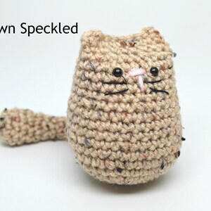 May include: A handmade crochet cat in brown speckled yarn. The cat has black eyes, whiskers, and a pink nose. The text "Brown Speckled" is above the cat.