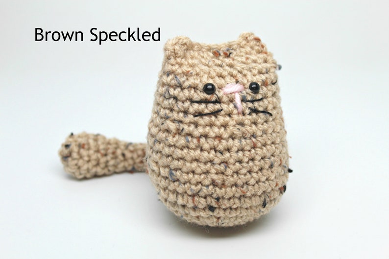 May include: A handmade crochet cat in brown speckled yarn. The cat has black eyes, whiskers, and a pink nose. The text "Brown Speckled" is above the cat.
