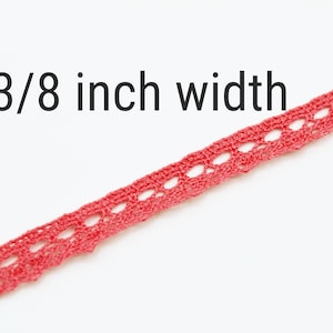 Könnte beinhalten: Nahaufnahme einer 3/8 Zoll breiten roten Häkelspitze. Die Spitze hat ein zartes Muster mit kleinen Löchern.