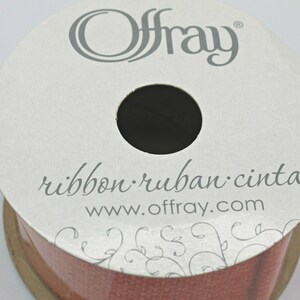 Pu&ograve; includere: Una bobina di nastro Offray in una tonalit&agrave; marrone rossastro. L'etichetta recita "ribbon ruban cinta" e "www.offray.com". Il nastro &egrave; ben avvolto, con un foro centrale. L'etichetta ha un design floreale.