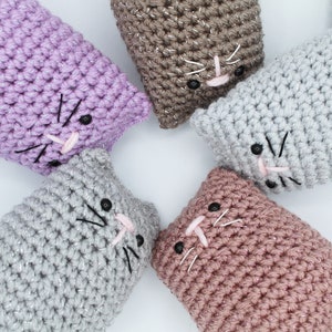 May include: Five crocheted cat toys in different colors, including purple, brown, gray, and pink. Each cat toy has a black embroidered face with pink nose and whiskers.