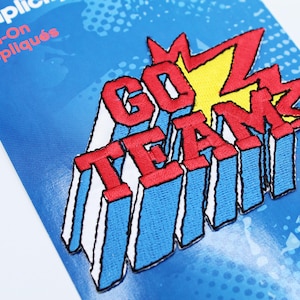 Può includere: Applique termoadesiva rossa e blu con il testo "GOZ TEAM" in stile fumetto.