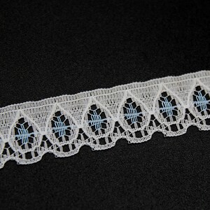 Puede incluir: Borde de encaje blanco con borde festoneado y detalles bordados azules.