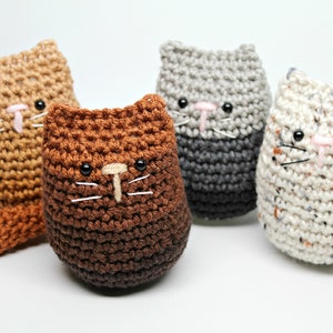 May include: Four handmade crochet cat toys in shades of brown, gray, and speckled white. Each cat has black eyes, a pink nose, and white whiskers. The cats are standing upright, with one cat having a tail.