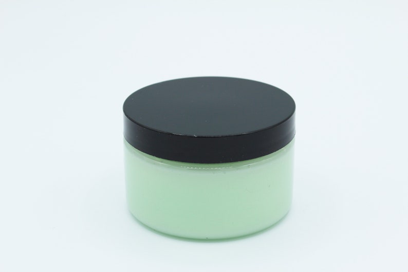 May include: A green jar with a black lid filled with a light green cream.