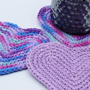 May include: Three crocheted heart-shaped coasters in shades of purple, pink, and blue. The coasters are made with a variety of stitches and are perfect for adding a touch of handmade charm to your home.