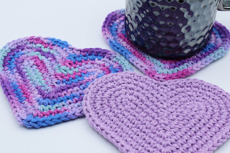 May include: Three crocheted heart-shaped coasters in shades of purple, pink, and blue. The coasters are made with a variety of stitches and are perfect for adding a touch of handmade charm to your home.