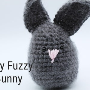 May include: Gray crocheted bunny with pink nose and black eyes. The bunny is sitting on a white surface. "Gray Fuzzy Bunny" is written in black text below the bunny.