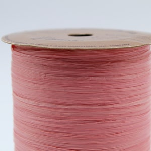 May include: A spool of pink paper ribbon. The ribbon is made of thin, crinkled paper and is wound around a cardboard spool.