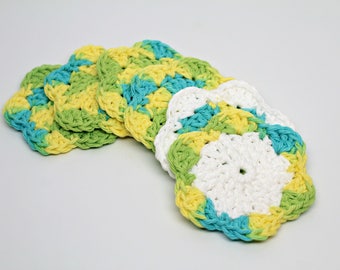 May include: A set of handmade crochet coasters in a flower shape. The coasters are in white, yellow, green, and turquoise. The crochet pattern is visible, adding texture and detail to the design. Each coaster is approximately 10 cm in diameter.