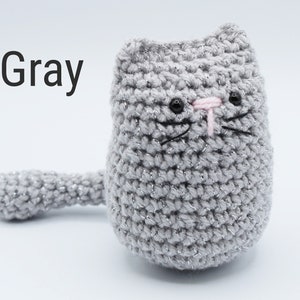 May include: Gray crocheted cat with pink nose and black eyes. The cat has a sparkly finish.