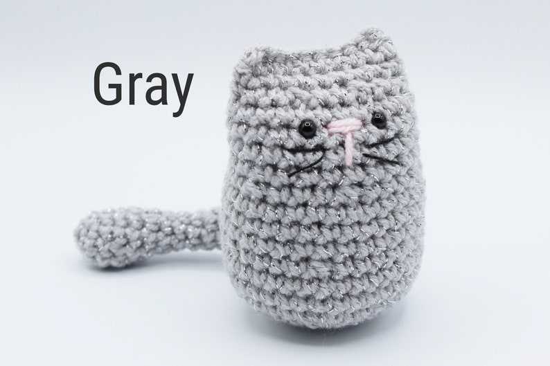 May include: Gray crocheted cat with pink nose and black eyes. The cat has a sparkly finish.