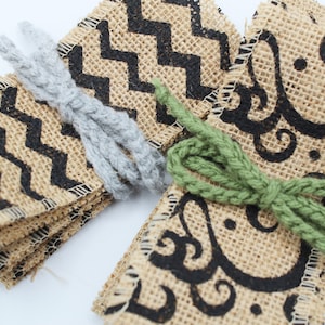 May include: A stack of burlap ribbon with black chevron and swirl patterns. The ribbon is tied with grey and green yarn.
