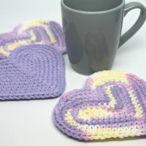 May include: Three crocheted heart-shaped coasters in shades of purple, pink, and yellow. The coasters are made with a soft, textured yarn and are perfect for protecting surfaces from heat and spills.