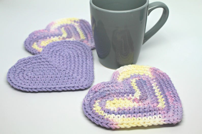 May include: Three crocheted heart-shaped coasters in shades of purple, pink, and yellow. The coasters are made with a soft, textured yarn and are perfect for protecting surfaces from heat and spills.